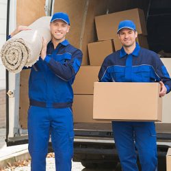 Portrait of happy delivery men carrying cardboard box and carpet outside van